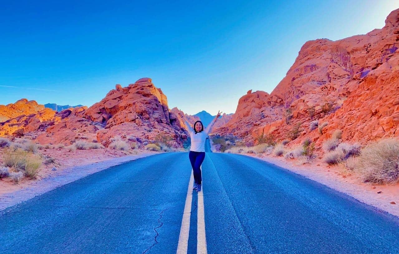 Girl posing with hands in the air with peace signs in the middle of the road on White Domes Road at Valley of Fire State Park