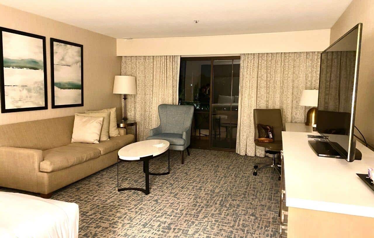 View of the hotel room with bed and sofa to the left and desk, chair and tv on dresser to the right at the Hilton Santa Barbara